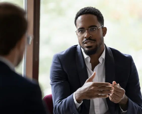 A black man in a suit talks with a colleague