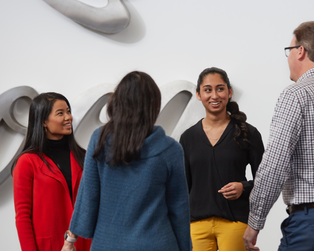 A diverse group of colleages chatting in front of a Coca-Cola logo backdrop