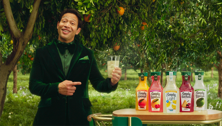 A Tuxedoed Eugene Cordero Holding a Glass of Simply Next to Bottles of Simply