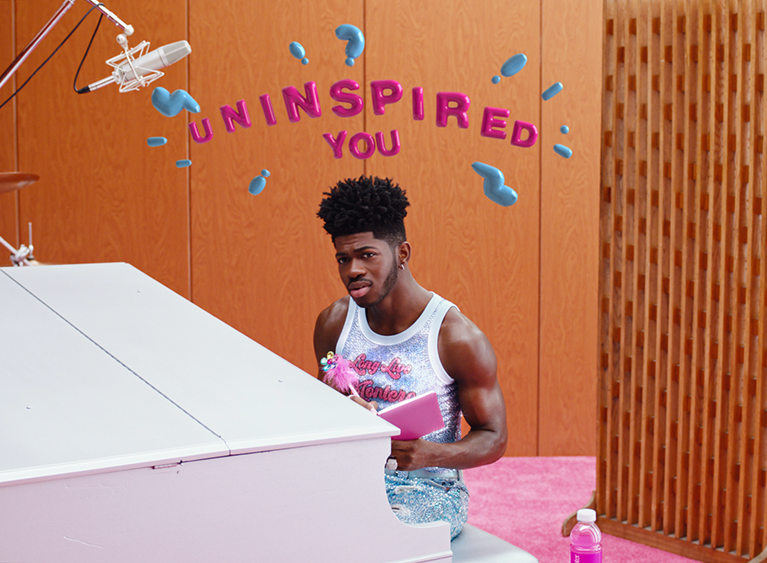 Lil Nas X Sits Uncertain at a Piano with the words "Uninspired You" Above Him