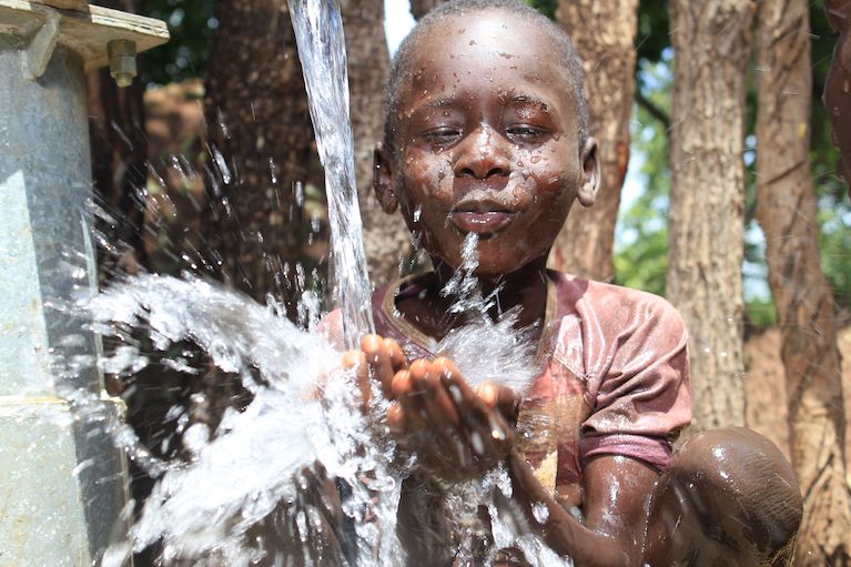 Young African boy cools off from outdoor water fountain developed through Coca-Cola's Replenish Africa Initiative.
