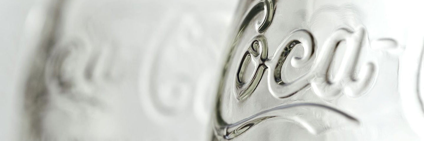 A close-up image of a clear, glass Coca-Cola bottle