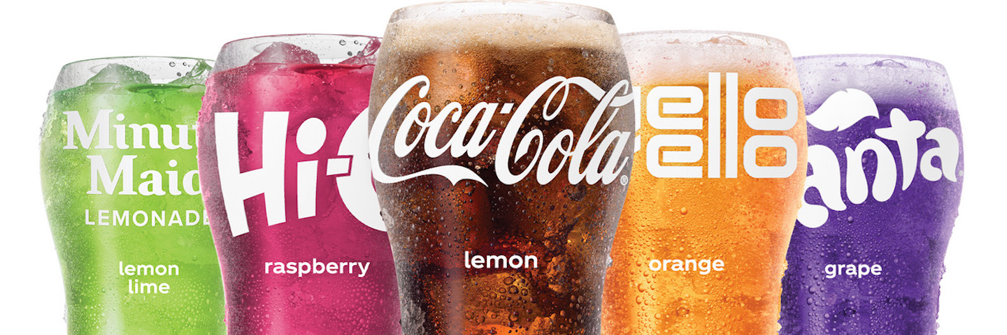 Lineup of 5 Coca-Cola Freestyle beverages in bell glasses Ribbon shape formed out of Coca-Cola Freestyle logos