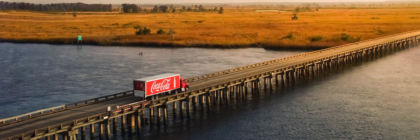 A Coca-Cola Semi Truck Driving Across a Bridge Over Water