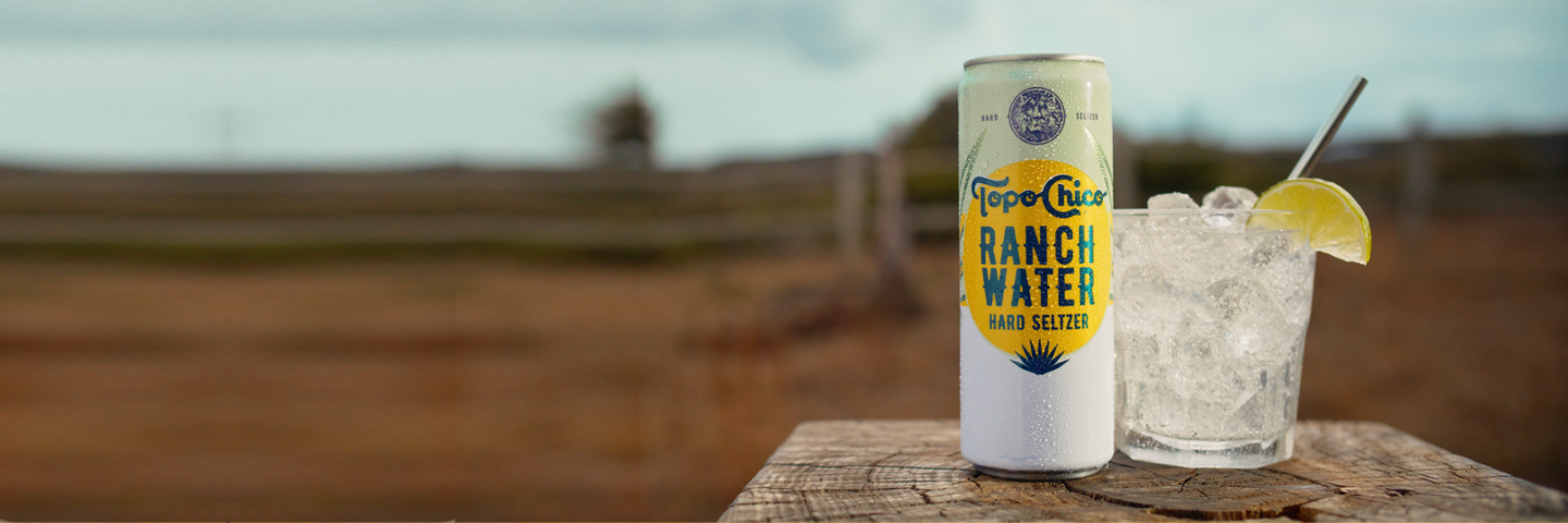 Topo Chico Ranch Water Hard Seltzer can with cocktail glass on a farm