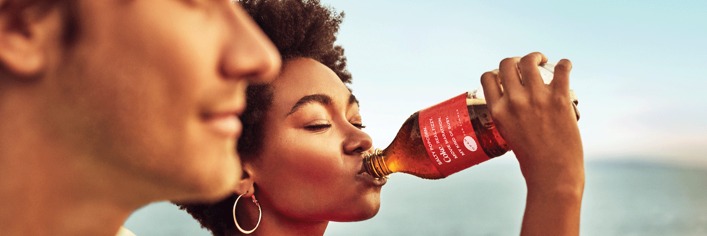 Woman drinks Coca-Cola summer bottle on beach with male