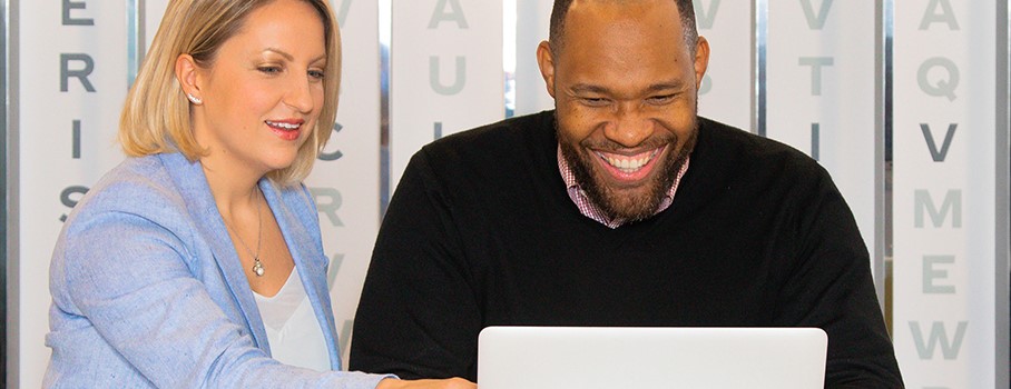 A man and woman smile as they look at a laptop