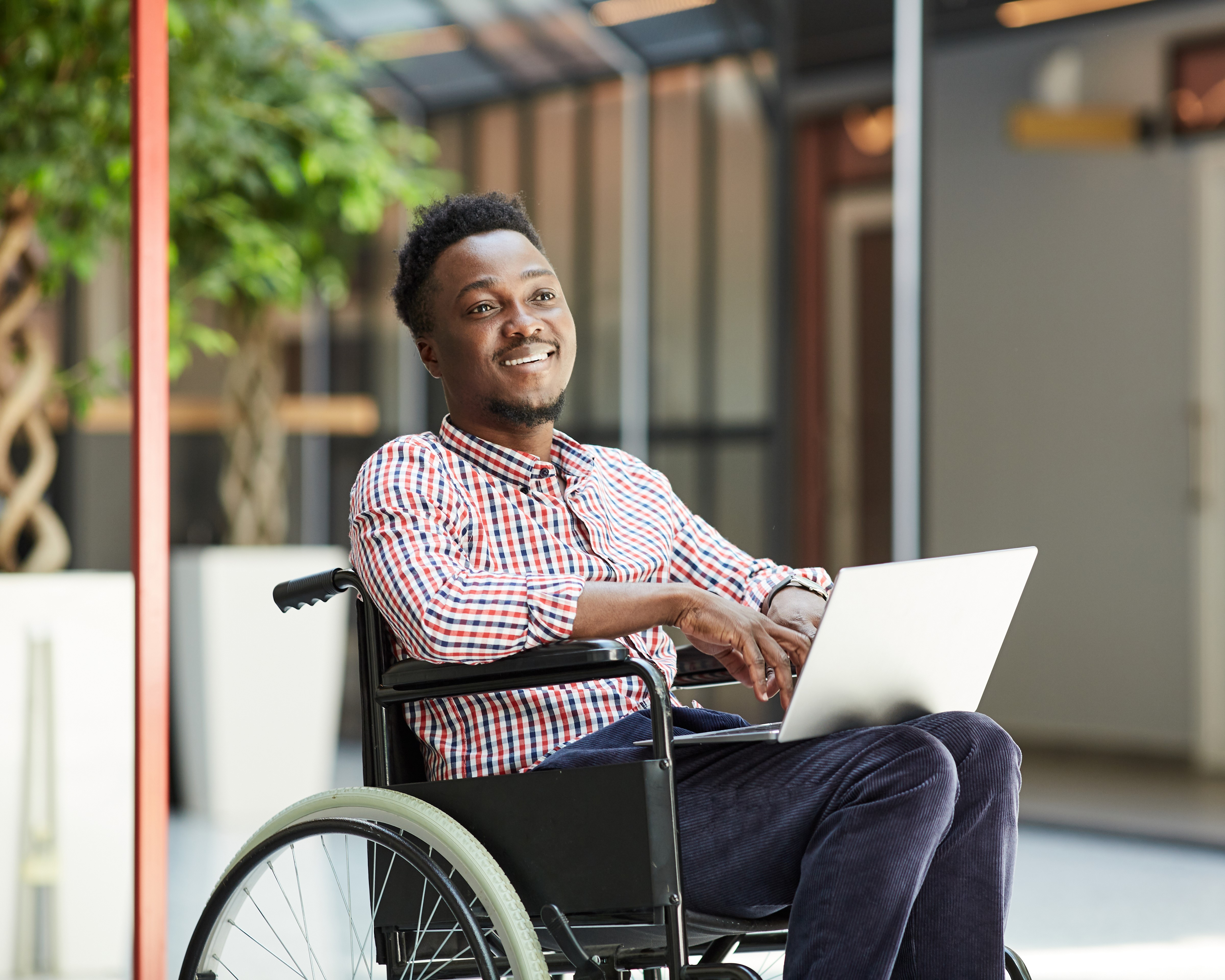 A man in a wheelchair smiles as he works from a laptop