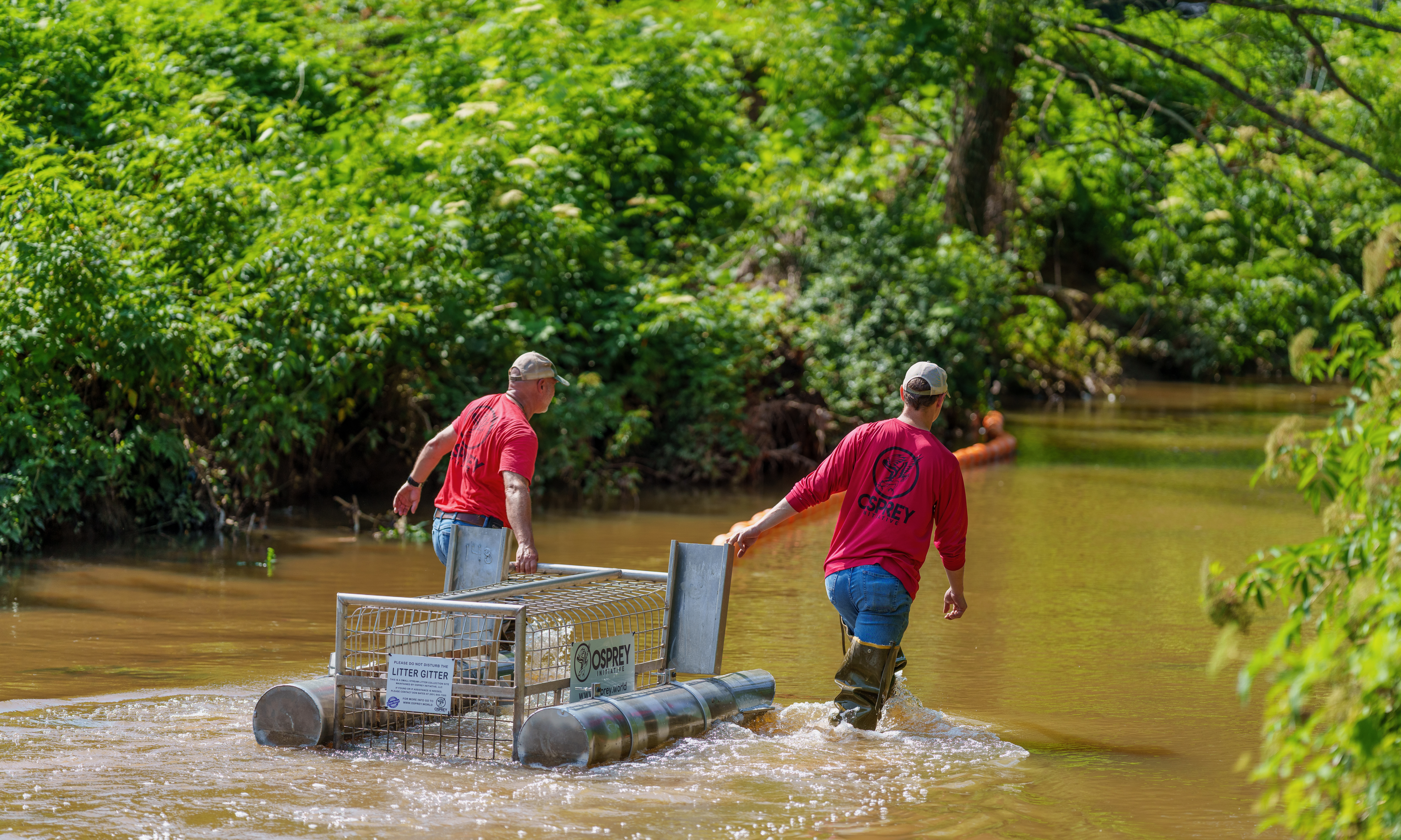 Osprey Initiative volunteers walk through water to place a Litter Gitter in position