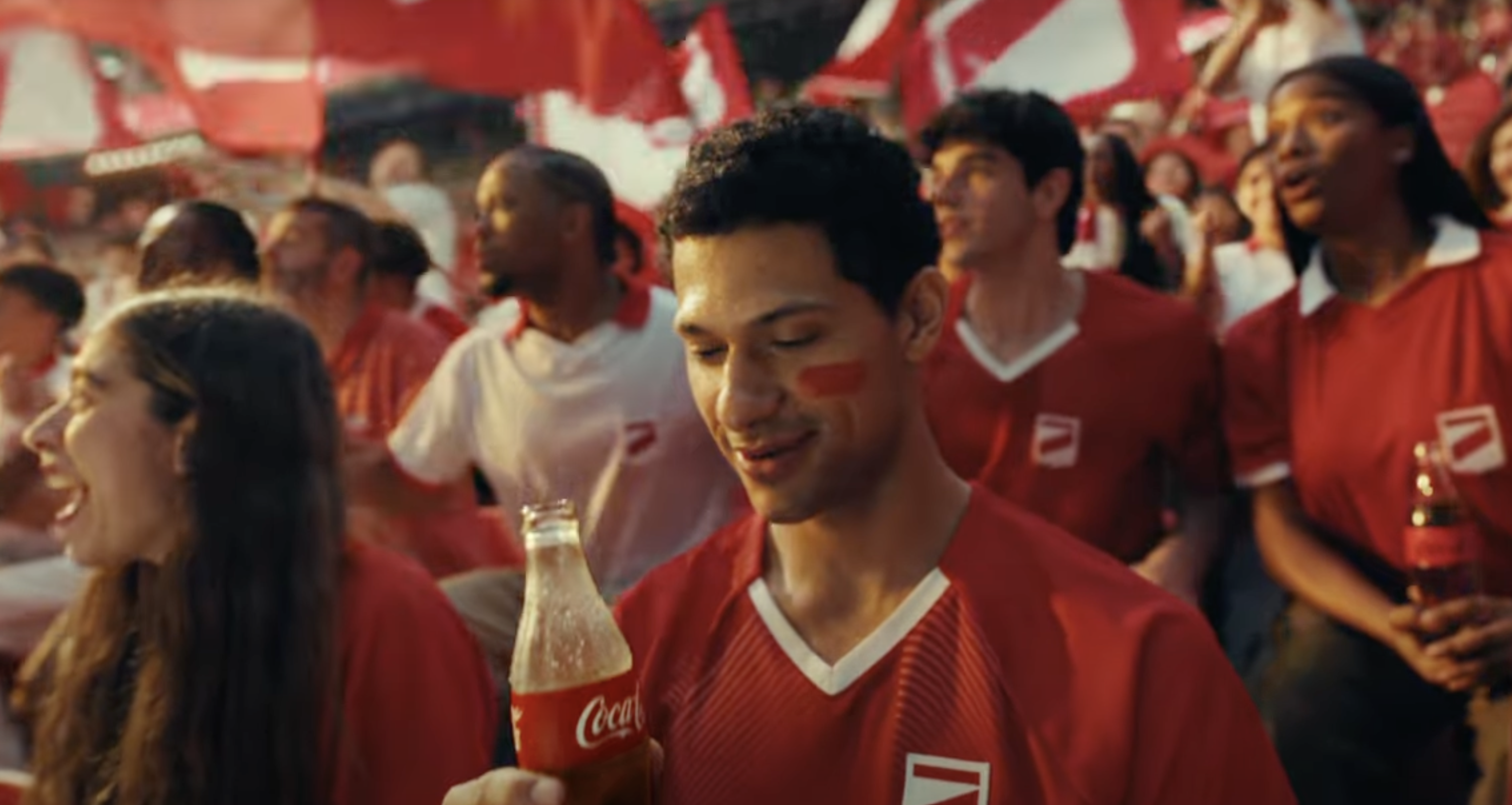 A stadium of fans cheer as a man looks at his Coca-Cola is held in the forefront