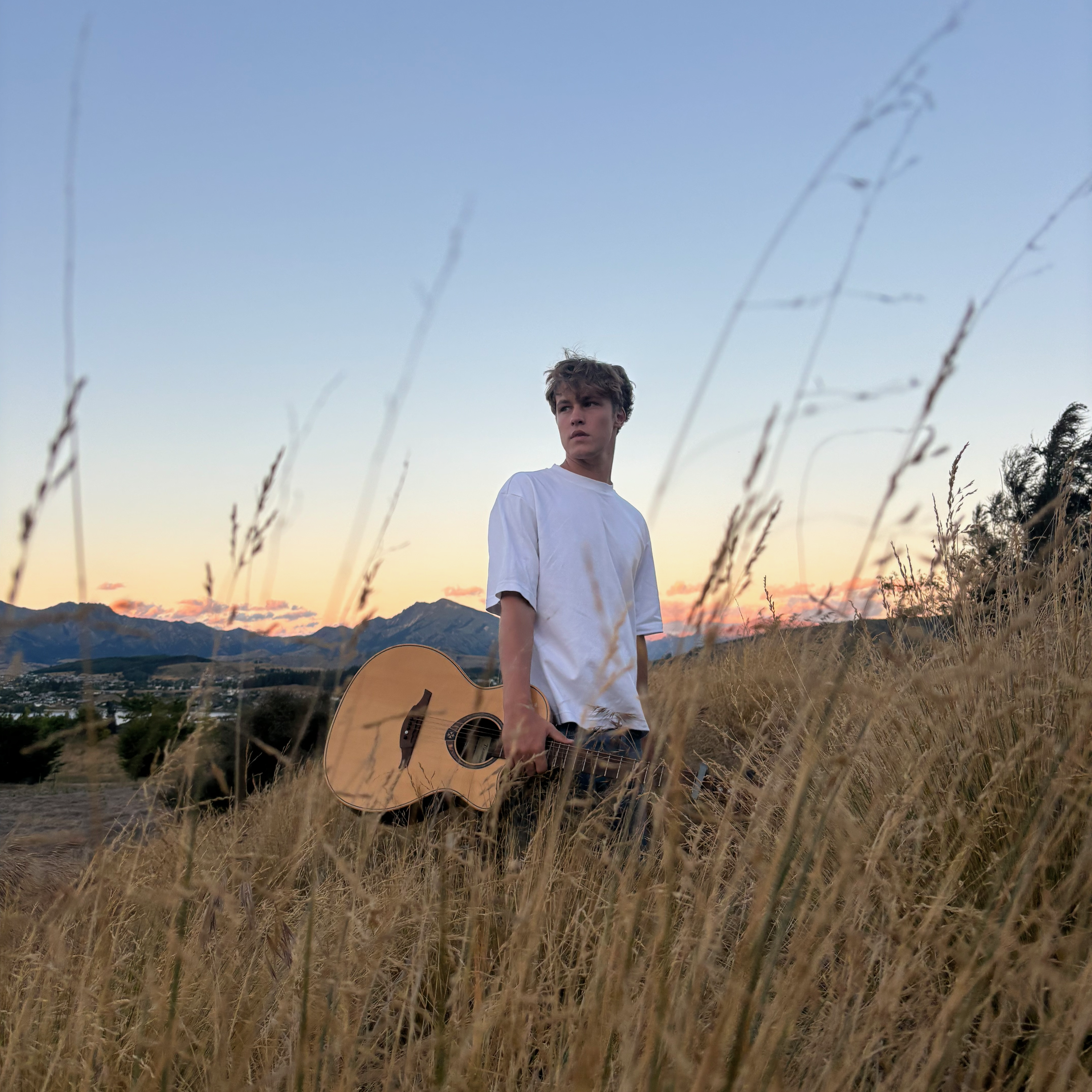 Max Allais holding a guitar in a field