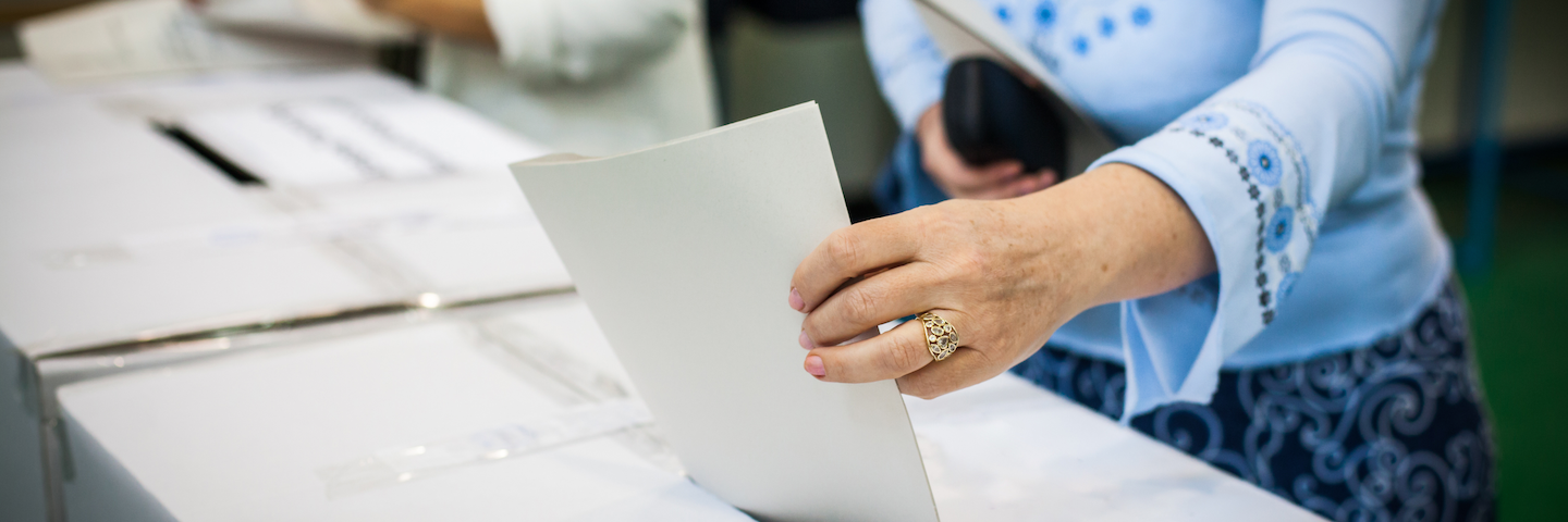 Woman's hand places election ballot into ballot box.