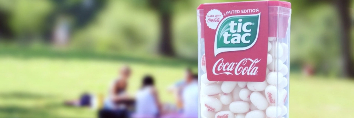 A pack of Tic Tacs made with Coca-Cola in front of a grassy park