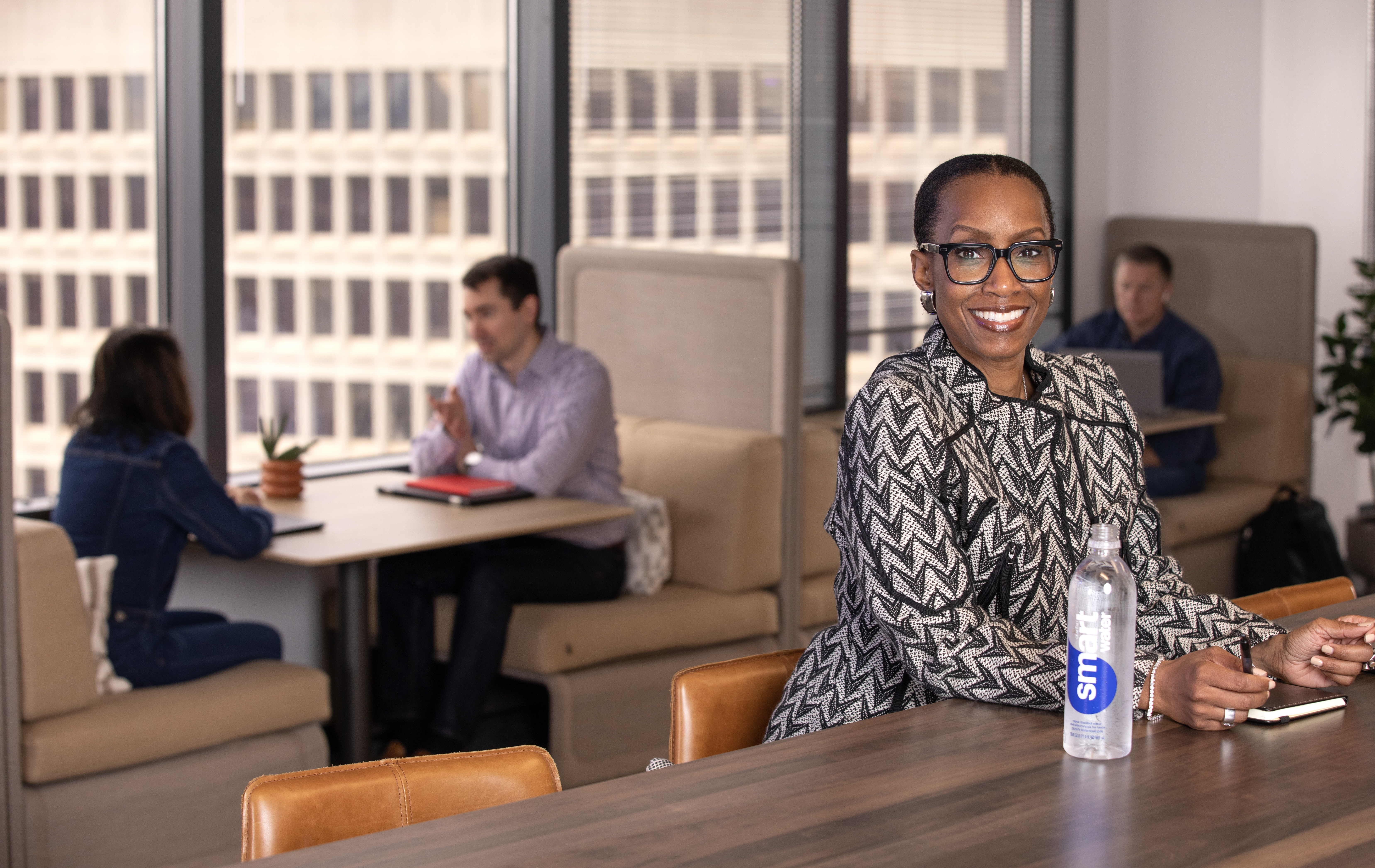 An employee smiles as other work in the background with a building skyline outside the windows