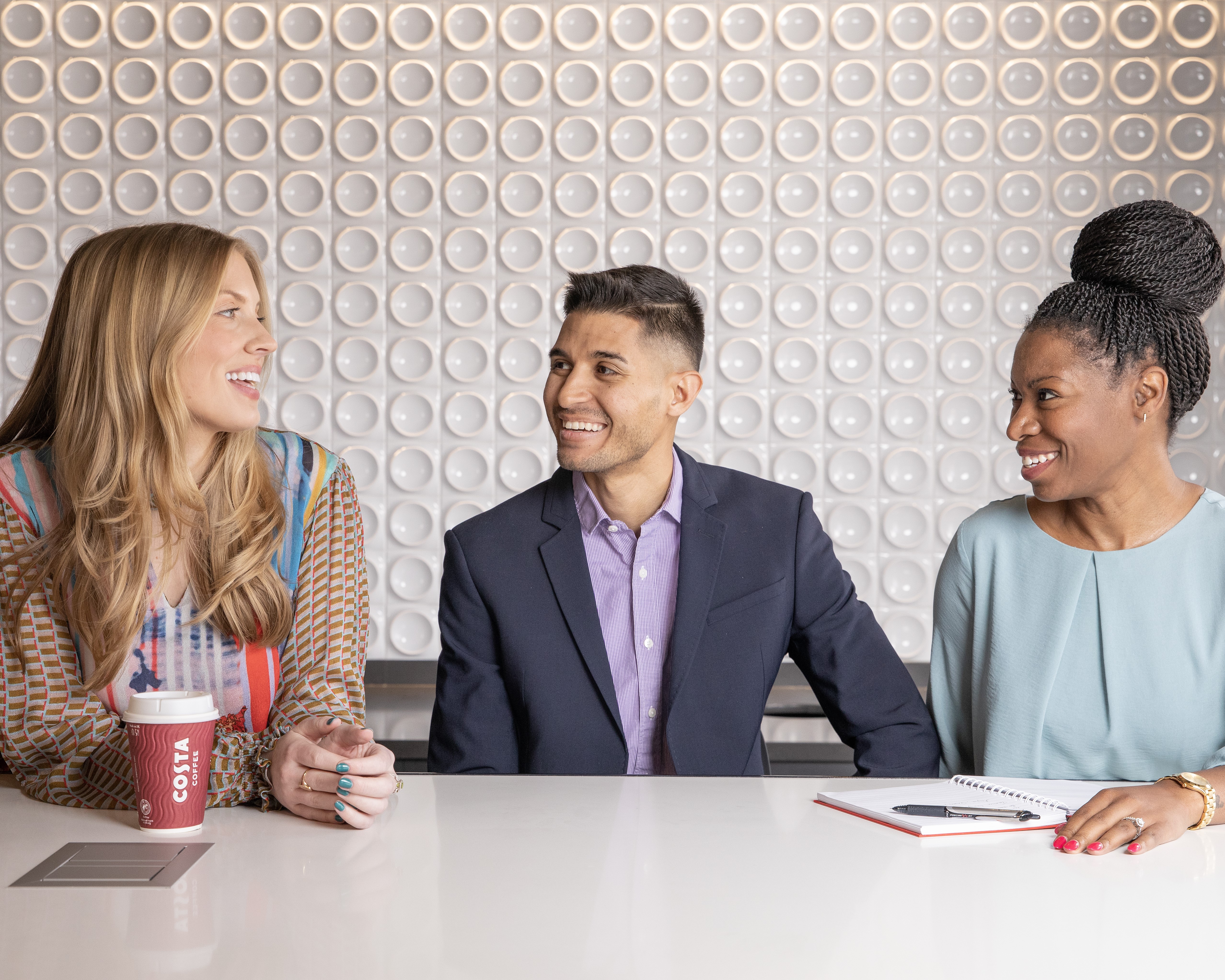 Three employees smile inbetween conversation