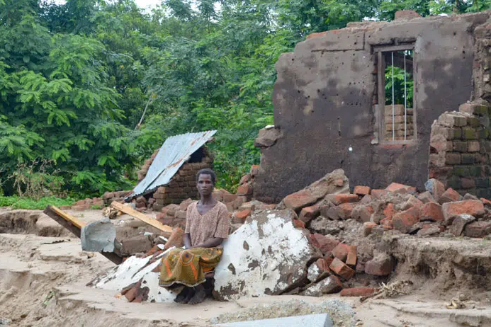 A woman sits facing camera with rubble behind her