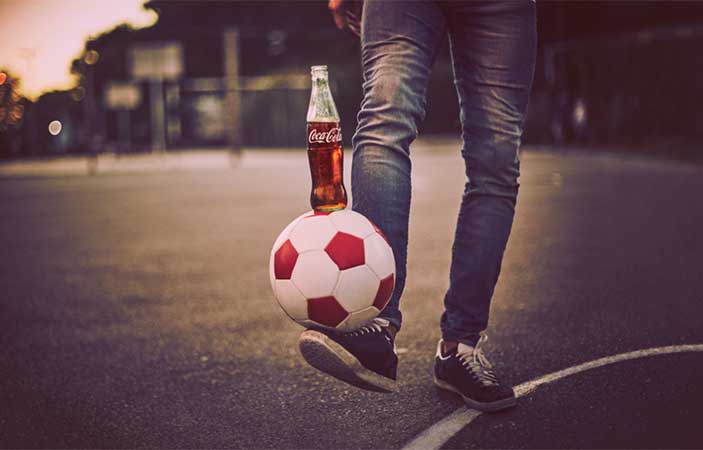 A Coke bottle ballanced on a soccer ball balanced on a foot