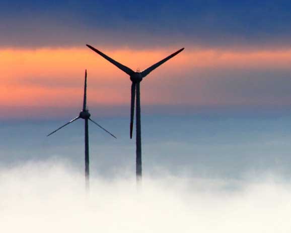 Energy-producing wind turbines rising above clouds