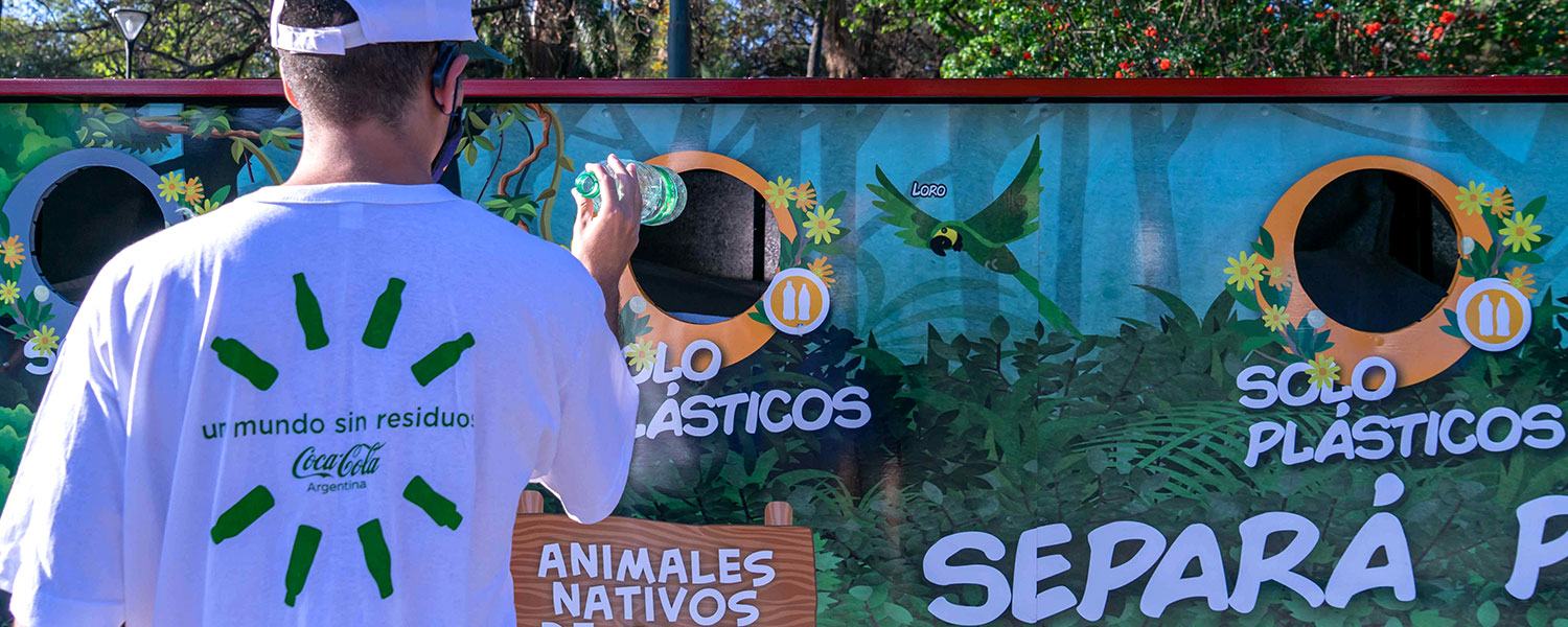 Man recycling plastic bottle of Sprite in large outdoor recycling bin