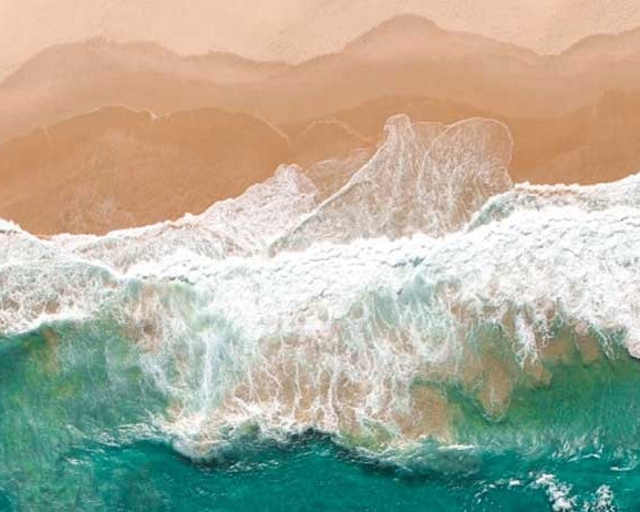 An overhead shot of ocean water splashing against sand