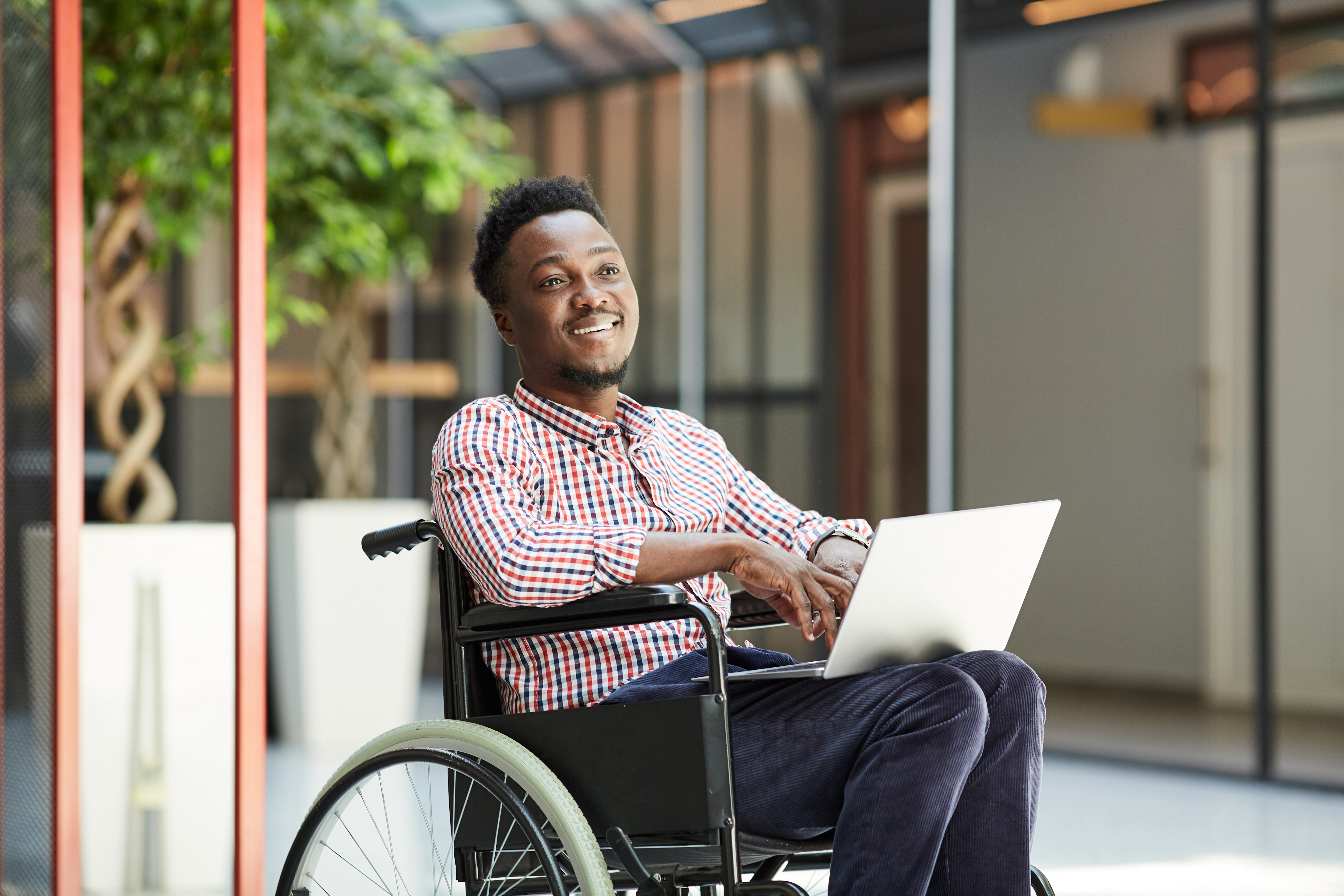 African smiling man sitting in wheelchair and using laptop computer in the mall