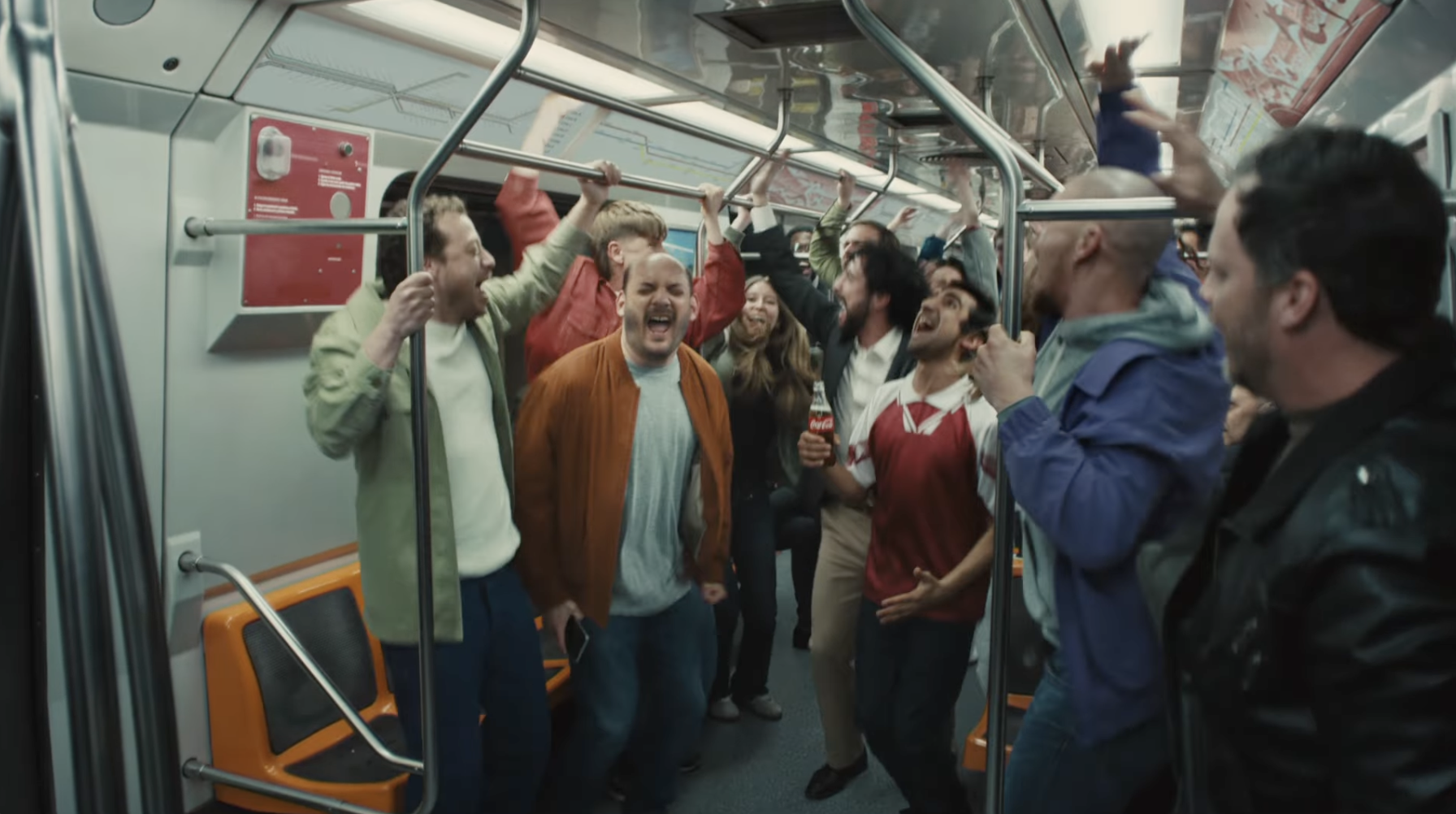 A still image from a Coca-Cola ad features soccer fans singing on a subway train
